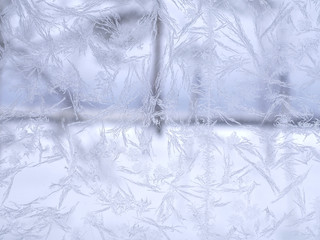 Beautiful frosty and icy window of forest cottage. Blurry scenery behind the glass.