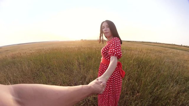 follow me. pretty portrait brunette girl goes with a man by the hand on nature field romance love. slow motion video. girl and lifestyle man walking call beckoning finger. follow me concept