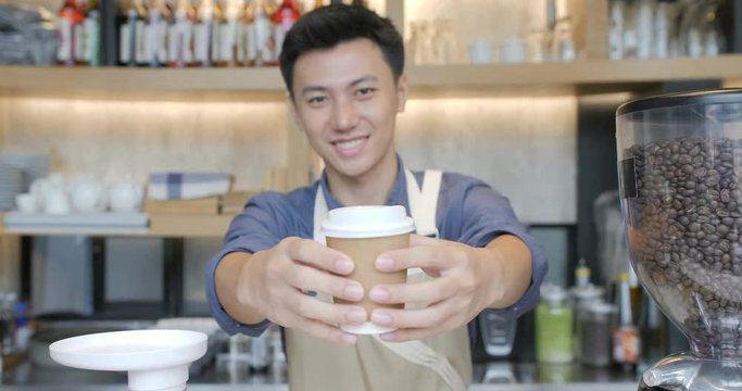 Coffee Business Concept - Beautiful Caucasian lady smiling at camera offers disposable take away hot coffee at the modern coffee shop