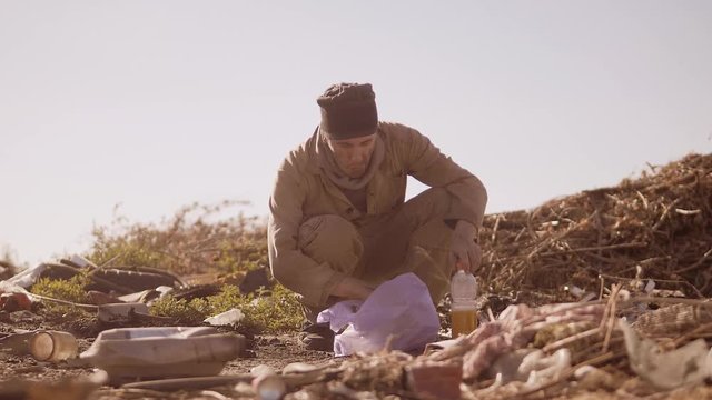 portrait of a dirty homeless hungry man in a dump eating for food in the package with walking goes looking for food slow motion video. homeless dirty man roofless person looking for food in a dump