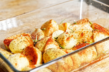 Preparing food - raw potatoes in rosemary, paprika and chili in glass dish on a wooden table prepared to be baked