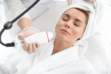 Naklejka premium Pleased woman having procedure with gadget in beauty salon. Worker making it with digital device