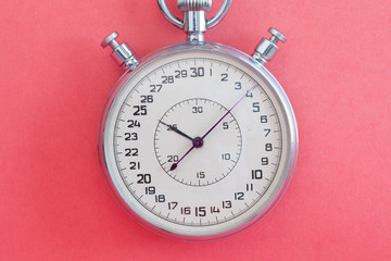 Retro style stopwatch chronometer on pink paper textured background. Sport competition time management concept. Macro view, soft focus