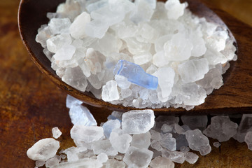 Persian blue salt crystal macro view. Mineral saline sodium chloride from Semnan Iran. Organic food condiment wooden spoon, aged rusty background. Shallow depth field.