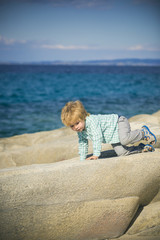 Climbing. A handsome active boy crawls on white stones. Rest near the sea. Summer trip. An active holiday. Happy summer near the sea. White child on vacation. Sport for children