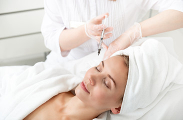 Portrait of pleased girl lying on bed during cosmetic procedure. She getting injection in check
