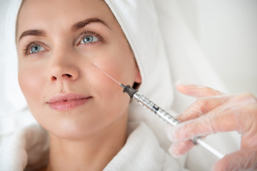 Positive lady during procedure in cosmetology clinic. Female hand in glove holding squirt gun