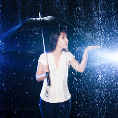 Woman under umbrella. Girl holding hand out to touch the raindrops