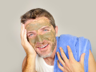 lifestyle isolated portrait of young attractive and happy man with bathroom towel  smiling with green cream on his face applying facial mask in skin care