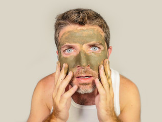  attractive and surprised funny man horrified looking himself on bathroom mirror ugly and weird applying green cream on his face in facial mask male beauty product