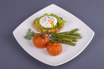 Poached egg on a piece of bread with fried green beans, tomato and arugula on a plate