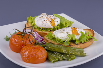 Poached egg on a piece of bread with fried green beans, tomato and arugula on a plate