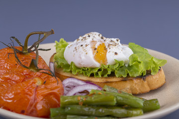 Poached egg on a piece of bread with fried green beans, tomato and arugula on a plate