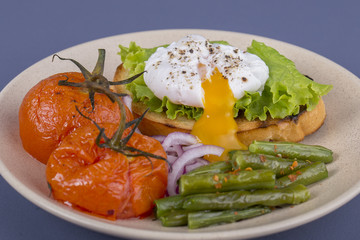 Poached egg on a piece of bread with fried green beans, tomato and arugula on a plate