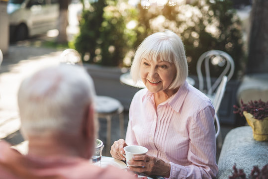 Waist up portrait of happy elderly lady communicating with male outside. They are drinking tea and enjoying evening together
