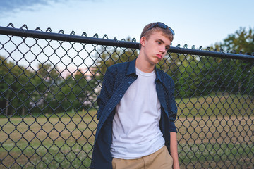 Sad teenager leaning against a chain link fence.