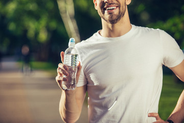 My choice. Close up of male hand holding bottle of liquid. Young guy is happily demonstrating it outdoors