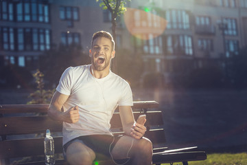 Yes. Waist up portrait of thrilled attractive male sitting outside and screaming in joy. He is...