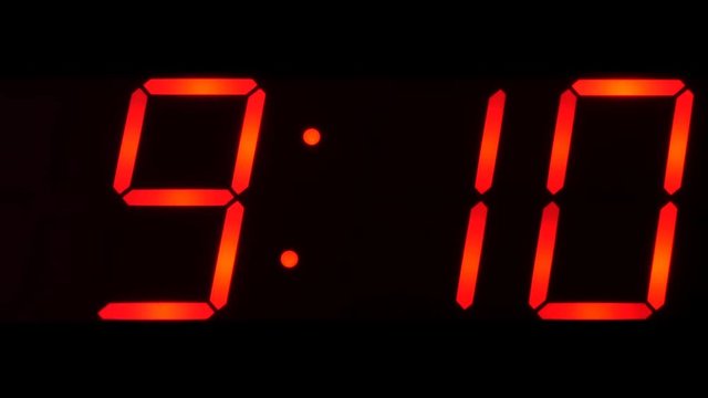 Close up of huge black, dark clock digital display, screen showing time between 9:00 and 9:59 o'clock and beyond in the morning or evening in big red digits
