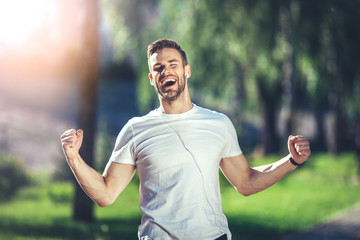 It is my life. Waist up portrait of smiling young man singing with earphones during jogging. He is...
