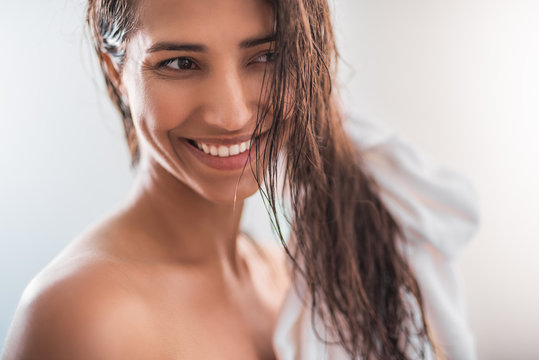 Portrait of satisfied female with brilliant smile keeping hair with towel