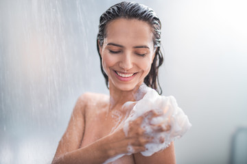 Portrait of happy girl taking shower with gel. She washing with puff - obrazy, fototapety, plakaty