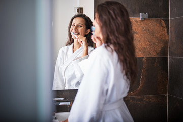 Naklejka premium Portrait of cheerful female brushing teeth while looking at mirror