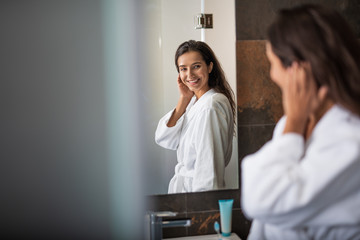 Portrait of cheerful girl watching at reflection in room. She holding cheek by hand