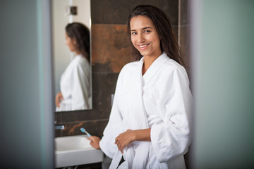 Portrait of beaming woman with attractive smile keeping toothbrush while looking at camera. She wearing fluffy bathrobe