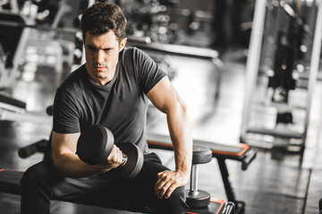 Fototapeta na wymiar Fit caucasian handsome young man and big muscle in sportswear. Young man holding dumbbell during an exercise class in a gym. Healthy sports lifestyle, Fitness concept.