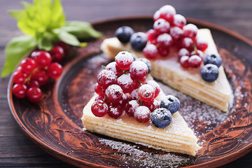 Two pieces of puff cake with fresh berries and sugar powder on brown plate and two brown cups of coffee on dark wooden table.