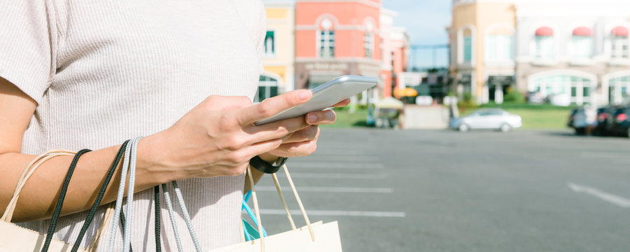 Young woman hold a shopping bags in her hand and chatting on her phone after shopping. Young Woman shopping in pastel town under the blue sky. Close up of outdoor shopping concept. Panoramic banner.