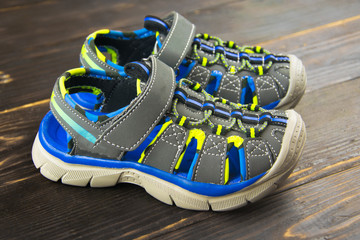closed sports sandals for the boy in blue-gray-yellow color on the  wooden surface