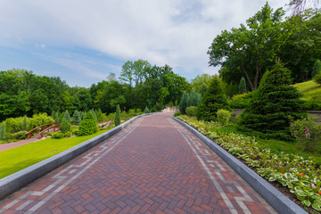 Alley with patterns on the sides goes through a green park with succulent bushes, grass and trees