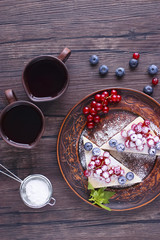 Two pieces of puff cake with fresh berries and sugar powder on brown plate and two brown cups of coffee on dark wooden table.