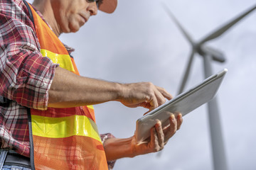 Senior electric engineer with safery helmet workingat wind mill or wind turbine power generator  station with tablet or clipboard..Clean energy concept.