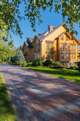 Fototapeta premium A beautiful summer day landscape in a park with a green lawn and a nearby path and a magnificent house of graceful architecture with a sheathed tree.