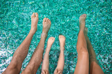 Top view of kid and adult legs swimming in pool. Happy parents and child relaxing on vacation