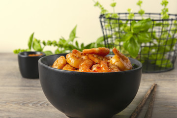 Fried shrimps in a black bowl. On a background basket with greens. Eastern food. Copy space.
