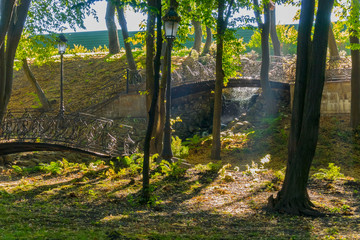The bridges in the park with figured forged fences and the rays of the sun making the trees through the foliage create a mystical atmosphere.