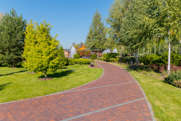 red track between planting trees and juicy green grass, leading to a fountain near the house. Novi Petrivtsi, Ukraine
