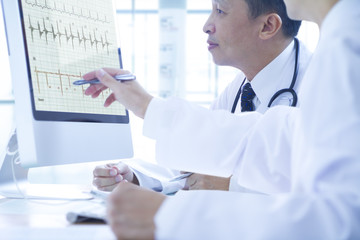 Asian doctors discuss to each other while analysing a patient’s health data on computer monitor.
