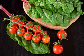 Cherry tomatoes on a dark table. Chard leaves in the background