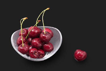 Washed sweet cherries on a black background. Prunus avium. Close-up of yummy fresh red berries of stone fruit in a glass bowl. Juicy vegetarian snack with beautiful water drops. Full depth of field.