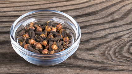 Close-up of spicy aromatic cloves in glass. Syzygium aromaticum. Decorative bowl with the pile of dried medicinal spices with distinctive scent on brown wood background. Great depth of field.