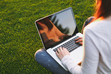 Close up hands on keyboard. Woman working on laptop pc computer with blank black empty screen to copy space in park on green grass sunshine lawn outdoors. Mobile Office. Freelance business concept.