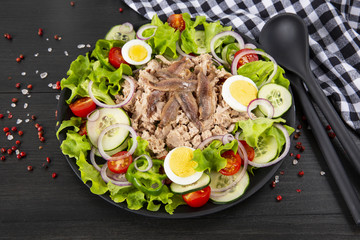 Salad with tuna, anchovies and vegetables. Mediterranean food. The background is black. Top view. Copy space. Horizontal shot.