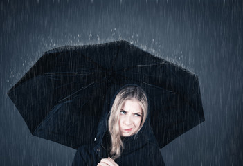 Junge Frau steht genervt unter Regenschirm im Regen