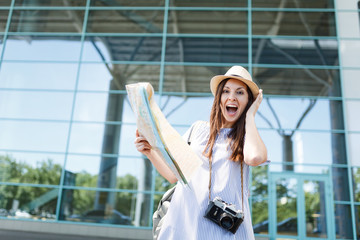 Young surprised traveler tourist woman with retro vintage photo camera, paper map, clinging to head at international airport. Female passenger traveling abroad on weekends getaway. Air flight concept.