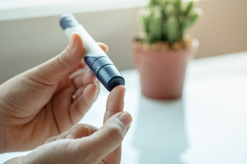 Close up of woman hands using lancet on finger to check blood sugar level by Glucose meter....